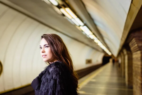 Элегантная женщина в искусственной меховой куртке смотрит в сторону, стоя на платформе метро — стоковое фото