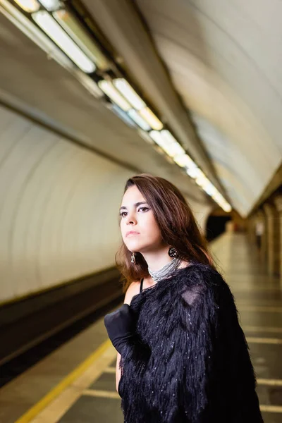 Mulher glamour em casaco de pele falso olhando para longe enquanto estava em pé na plataforma subterrânea — Fotografia de Stock