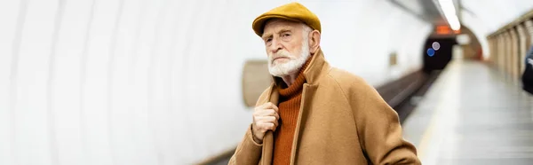 Homme âgé touchant le col du manteau tout en se tenant debout sur la plate-forme de métro, bannière — Photo de stock