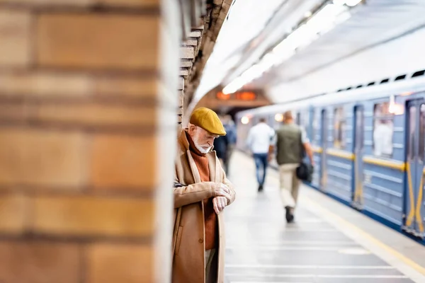 Senior en manteau d'automne et bonnet debout sur la plate-forme souterraine au premier plan flou — Photo de stock