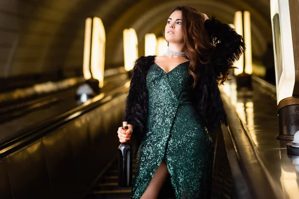 Vue recadrée de glamour femme posant sur escalator avec bouteille de vin — Photo de stock