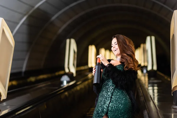 Ausgeschnittene Ansicht einer Glamour-Frau, die auf Rolltreppe mit einer Flasche Wein posiert — Stockfoto