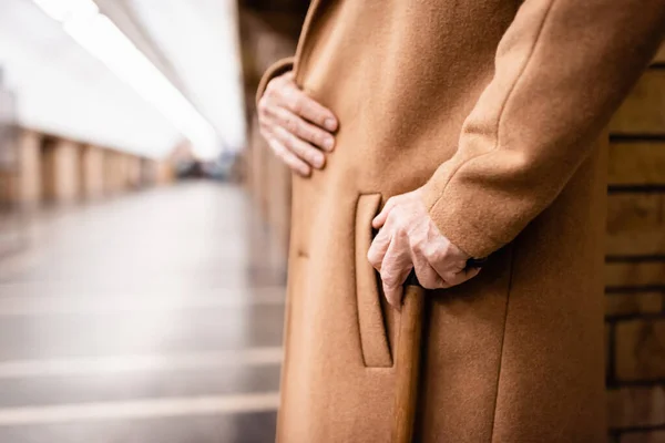 Vue partielle de l'homme âgé en manteau debout avec bâton de marche à la station de métro — Photo de stock