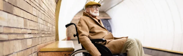 Elderly disabled man in autumn outfit and eyeglasses sitting in wheelchair on underground platform, banner — Stock Photo