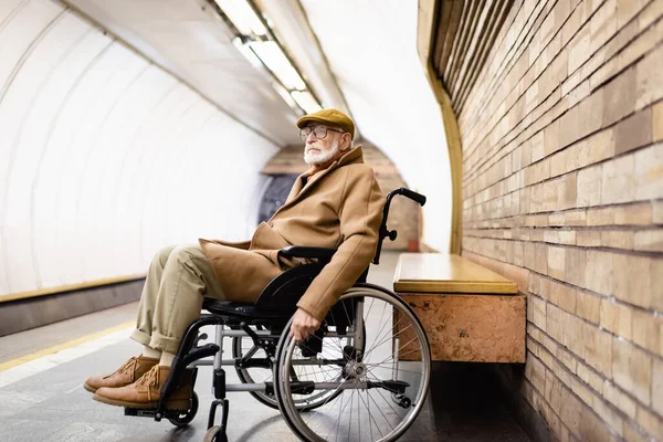 Aged disabled man in autumn clothes sitting in wheelchair on underground platform — Stock Photo