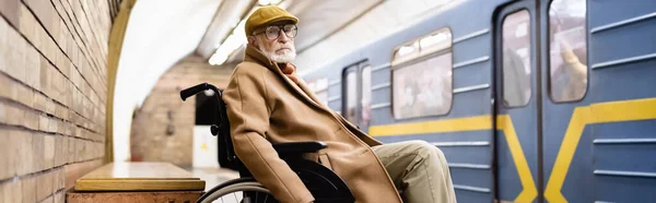 Elderly disabled man in wheelchair, wearing autumn clothes, near train on subway platform, banner — Stock Photo