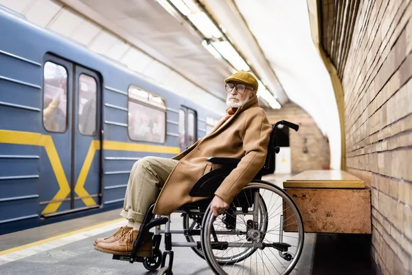 Старший інвалід у інвалідному візку, одягнений в осіннє вбрання, біля поїзда на платформі метро — стокове фото