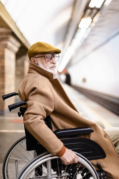 Homme handicapé âgé en manteau et casquette d'automne assis en fauteuil roulant sur la plate-forme du métro — Photo de stock