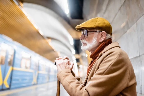 Vista laterale dell'uomo anziano in abiti autunnali e occhiali sulla piattaforma della metropolitana con treno sfocato — Foto stock