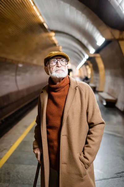 Uomo anziano in cappotto autunno e cappuccio guardando lontano sulla piattaforma sotterranea — Foto stock