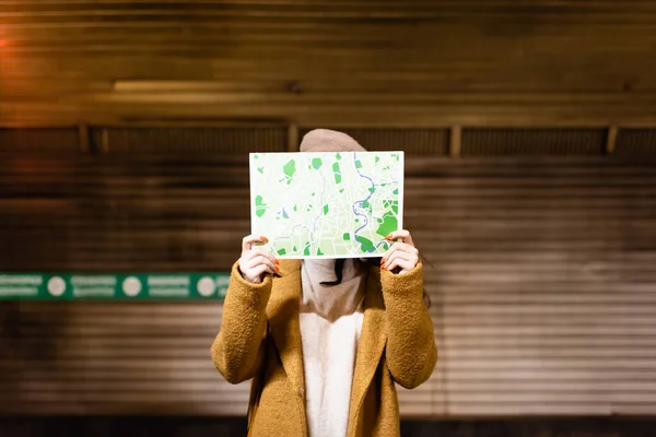 Женщина в осеннем пальто скрывает лицо с картой города на станции метро — стоковое фото