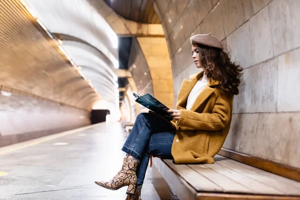 Stylische Frau in Baskenmütze und Herbstkleidung liest Magazin auf U-Bahn-Bahnsteig — Stockfoto