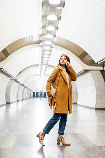 Молода жінка в стильному осінньому одязі розмовляє на мобільному телефоні на підземній станції — стокове фото