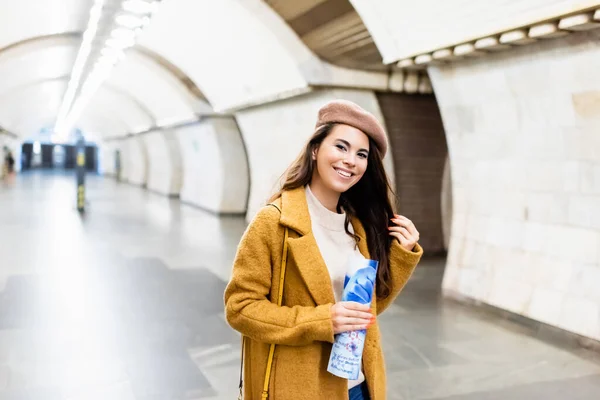 Cheerful woman in stylish autumn outfit holding magazine at underground station — Stock Photo