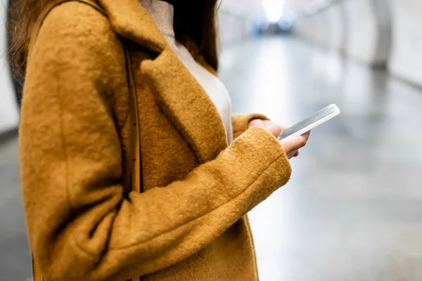 Partial view of woman in coat messaging on mobile phone on blurred foreground — Stock Photo