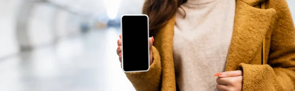 Cropped view of woman in autumn coat holding smartphone with blank screen, banner - foto de stock