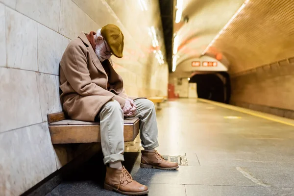 Elderly man in autumn outfit sleeping on subway platform bench - foto de stock