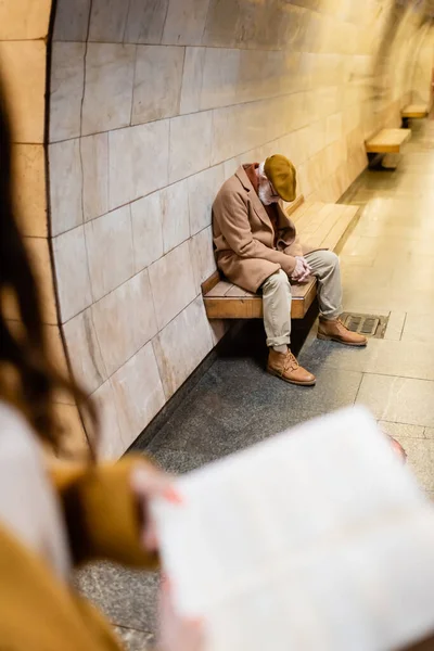 Senior im Herbst-Outfit schläft auf U-Bahn-Bahnsteigbank im verschwommenen Vordergrund — Stockfoto