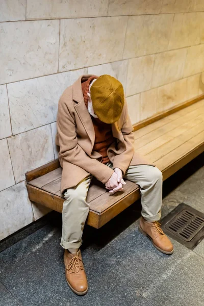 Uomo anziano in cappotto autunnale e cappuccio che dorme sulla panchina della piattaforma sotterranea — Foto stock