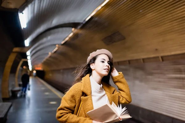 Donna elegante in autunno vestiti che tengono libro e guardando lontano sulla piattaforma della metropolitana — Foto stock