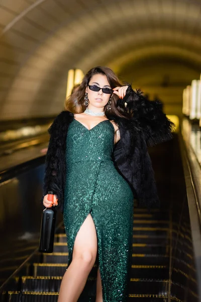 Vista cortada de mulher glamour posando na escada rolante com garrafa de vinho — Fotografia de Stock