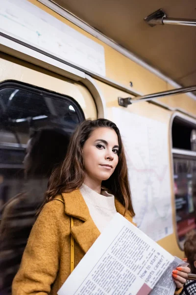Junge Frau mit Zeitung blickt während Fahrt in U-Bahn in Kamera — Stockfoto