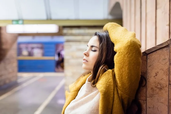 Jovem mulher em casaco de outono posando com os olhos fechados na estação de metrô — Fotografia de Stock