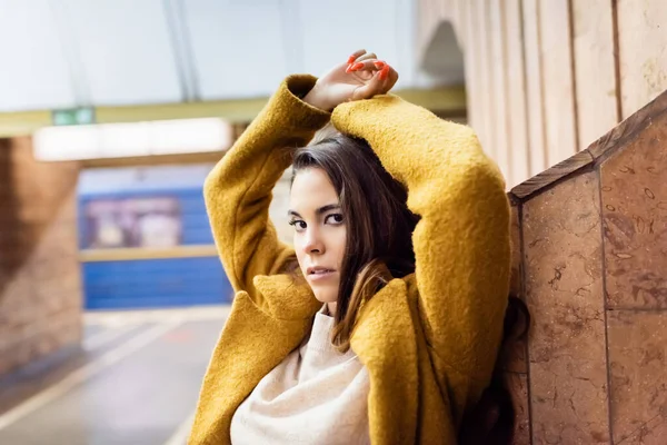 Jeune femme élégante regardant la caméra tout en posant près du mur à la station de métro — Photo de stock