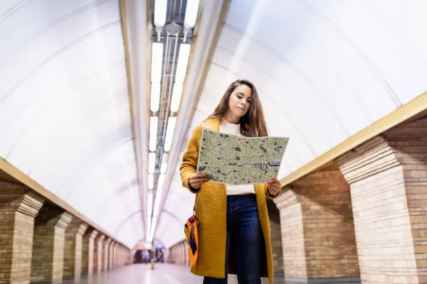 Jovem mulher elegante em roupas de outono olhando para o mapa da cidade na estação de metro — Fotografia de Stock
