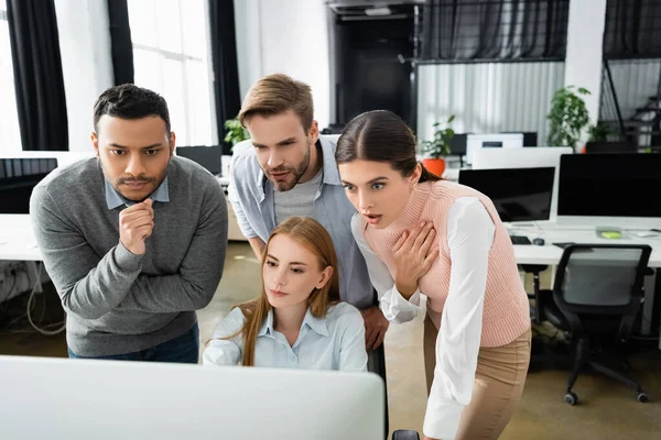 Aufgeregte multiethnische Geschäftsleute blicken im Büro auf den Computermonitor im verschwommenen Vordergrund — Stockfoto