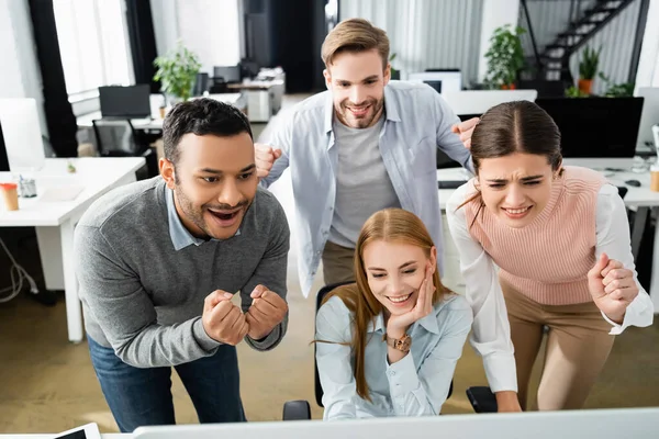 Excited multicultural businesspeople looking at computer on blurred foreground in office — Stock Photo
