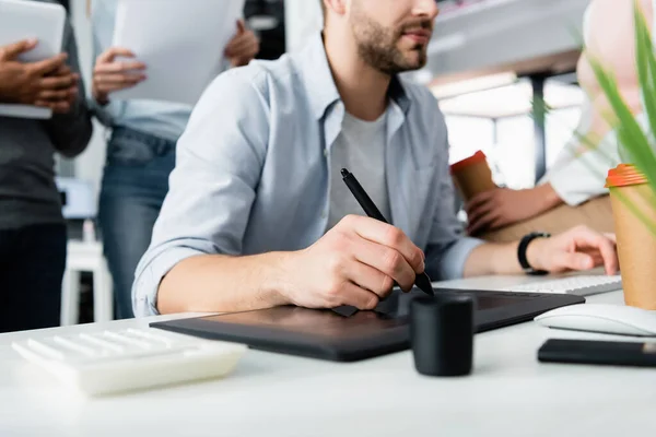 Vista recortada del hombre de negocios utilizando gráficos tableta y teclado de la computadora cerca de colegas en la oficina - foto de stock