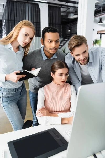 Entrepreneurs multiculturels avec ordinateur portable regardant près de tablette graphique sur le premier plan flou dans le bureau — Photo de stock