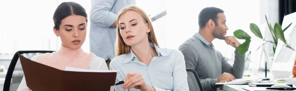 Empresarias mirando papeles cerca de colega indio en la oficina, pancarta - foto de stock