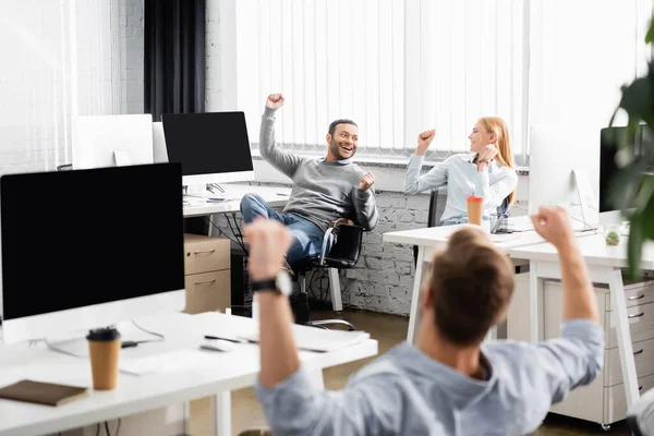 Multiethnische Geschäftsleute zeigen Yah-Geste, während sie in der Nähe von Computern im Büro arbeiten — Stockfoto