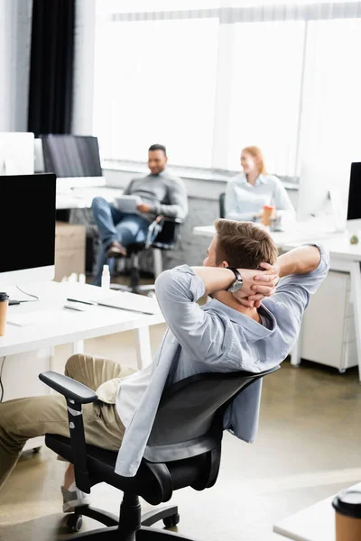 Empresario sentado cerca de la computadora y colegas en un fondo borroso en la oficina - foto de stock