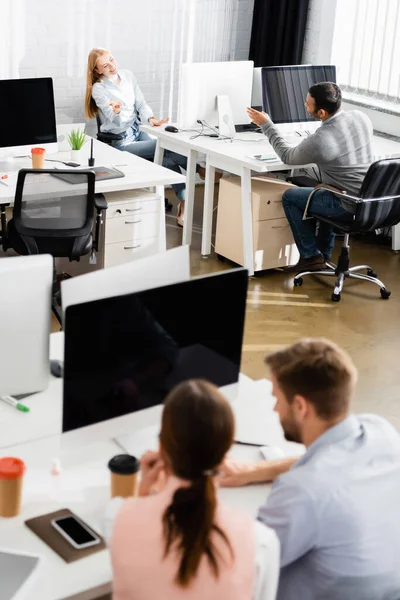 Empresários multiétnicos sorridentes conversando enquanto usam computadores no escritório — Fotografia de Stock