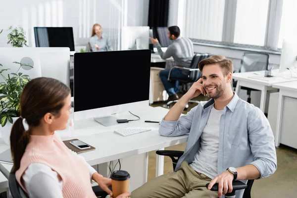 Uomo d'affari sorridente guardando collega con il caffè per andare in primo piano offuscata in ufficio — Foto stock