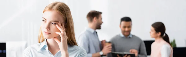 Umsichtige Geschäftsfrau, die in der Nähe von Kollegen auf verschwommenem Hintergrund im Büro wegschaut, Banner — Stockfoto