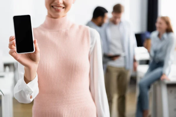 Cropped view of smiling businesswoman holding smartphone with blank screen on blurred background — Stock Photo