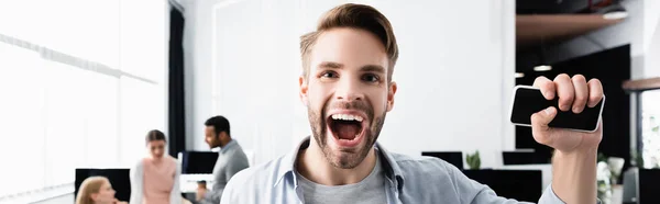 Empresário alegre segurando smartphone no escritório, banner — Fotografia de Stock