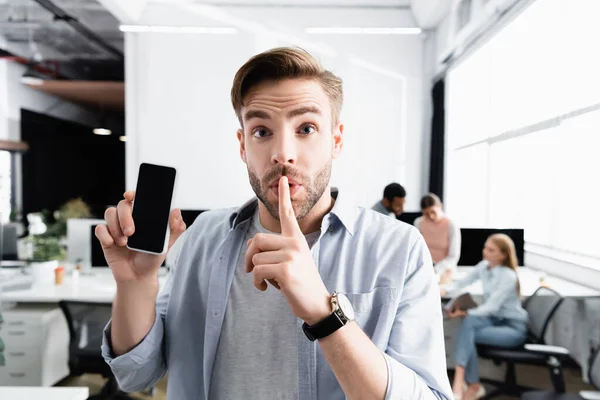 Businessman showing smartphone with blank screen and quiet sign in office — Stock Photo