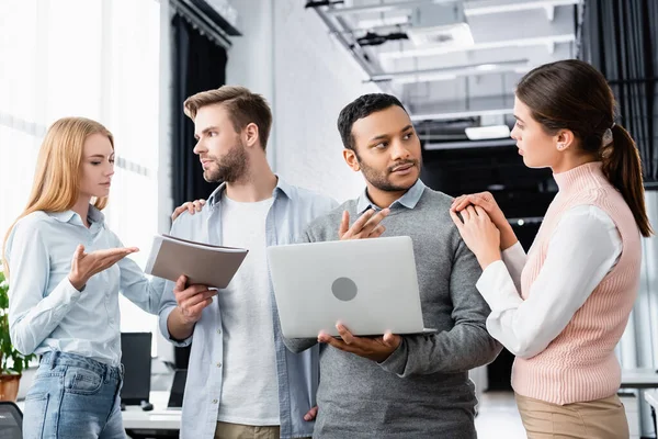 Empresarios multiétnicos trabajando con laptop y carpeta de papel en la oficina - foto de stock