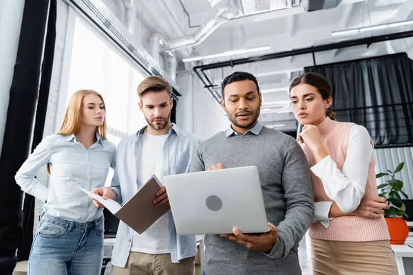 Multicultural businesspeople working with laptop and paper folder in office — Stock Photo