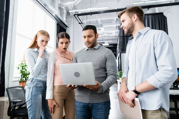 Geschockte Geschäftsleute schauen auf Laptop in der Nähe indischer Geschäftsmann im Amt — Stockfoto