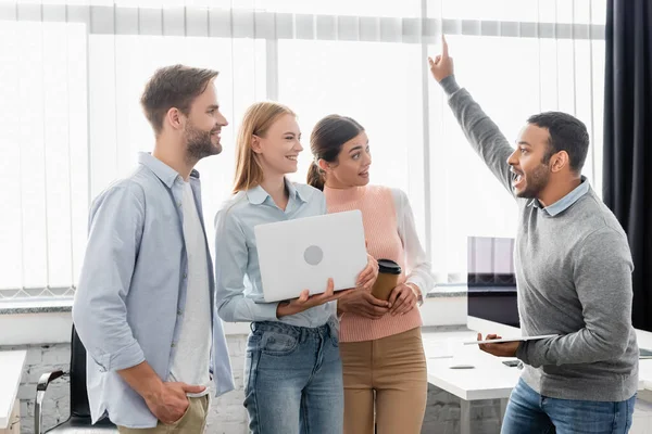 Emocionado empresario indio que tiene idea mientras sostiene la tableta digital cerca de colegas con computadora portátil - foto de stock