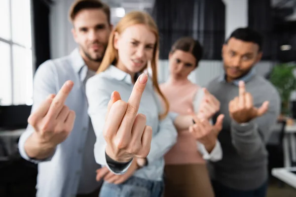 Multicultural businesspeople on blurred background showing middle fingers in office — Stock Photo