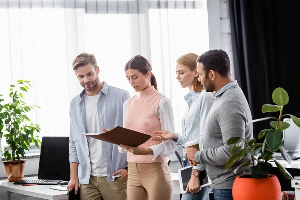 Multiethnic businesspeople looking at paper folder while working in office — Stock Photo