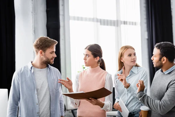 Multiethnische Geschäftsleute gestikulieren, während sie im Büro mit Papiermappe und digitalem Tablet arbeiten — Stockfoto