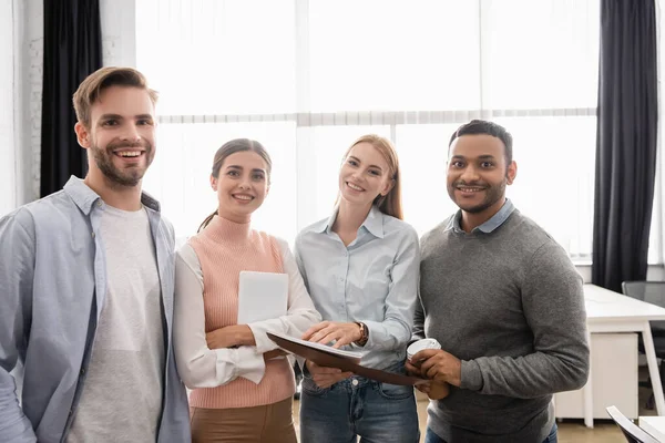 Empresários multiétnicos com pasta de papel e tablet digital sorrindo para a câmera no escritório — Fotografia de Stock